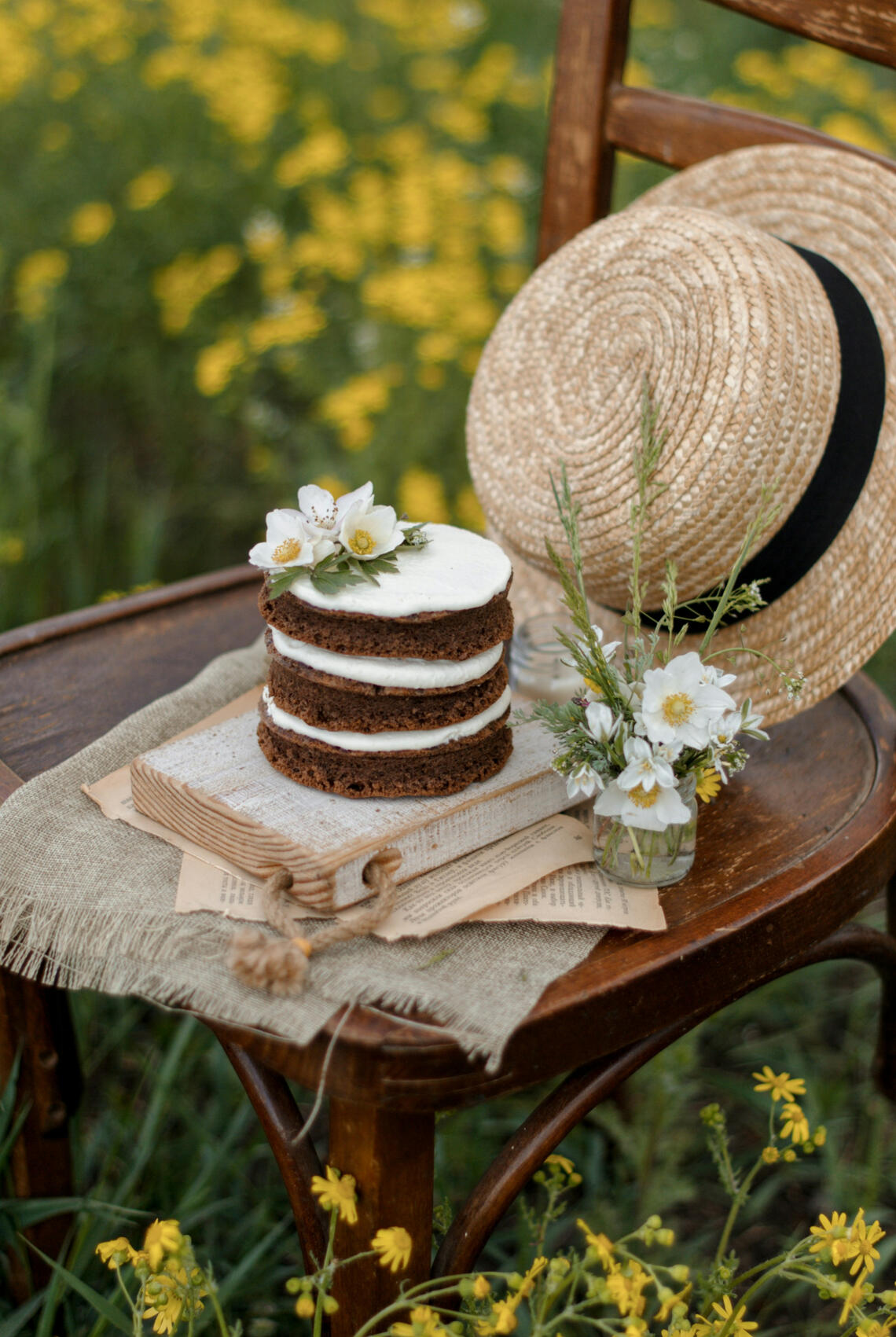 Photo by Kateryna Hliznitsova on Unsplash Small layered cake and straw hat on a brown chair surrounded by yellow flowers