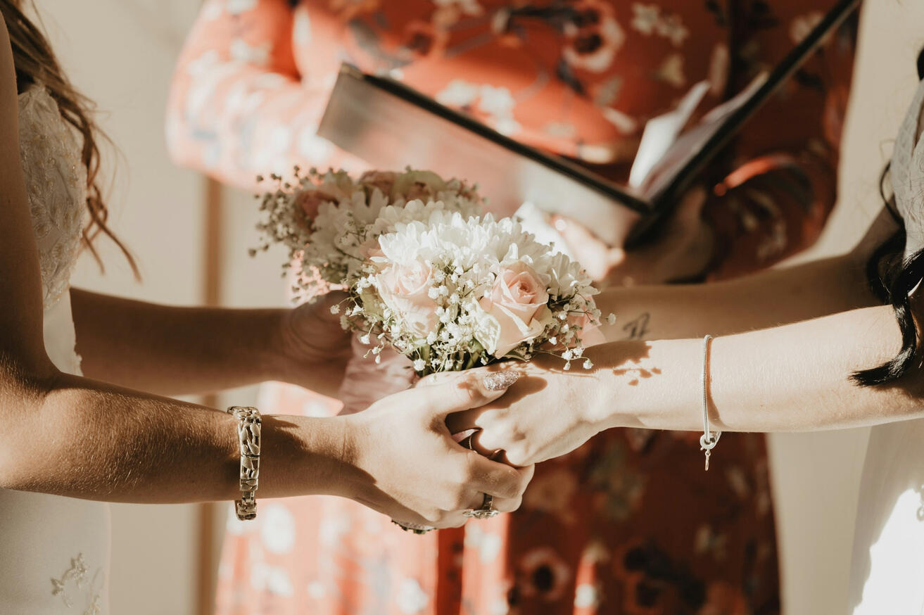 Photo by Sophia Hernandez on Unsplash Two brides holding hands around white floral bouquets