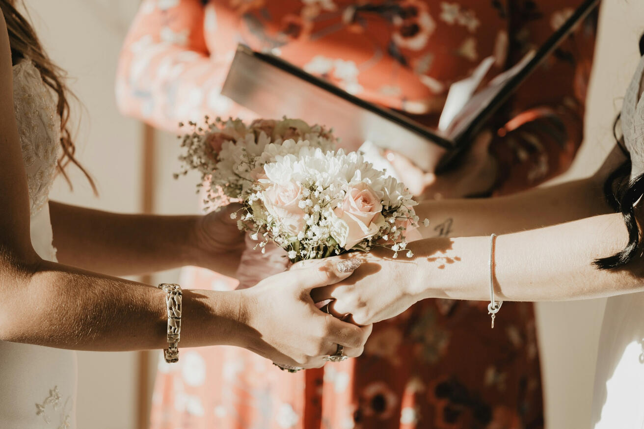 Photo by Sophia Hernandez on Unsplash Two brides holding hands around white floral bouquets